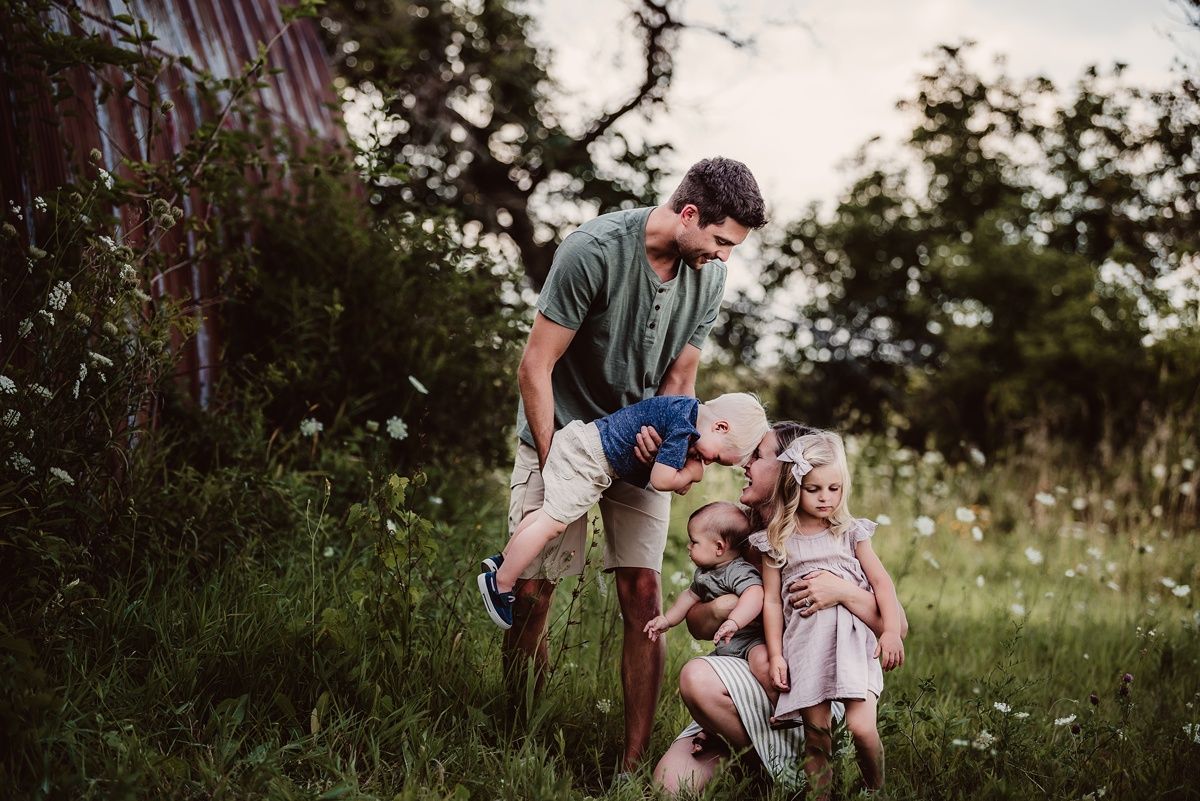 Family walking together through a wildflower field near a rustic barn structure.