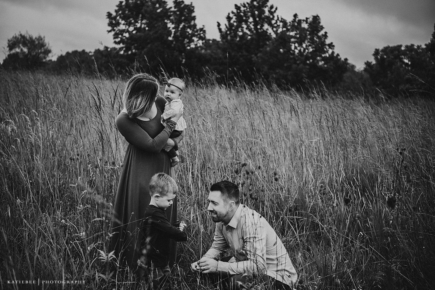 Black and white portrait of a family sharing an intimate moment in a tall grass field.