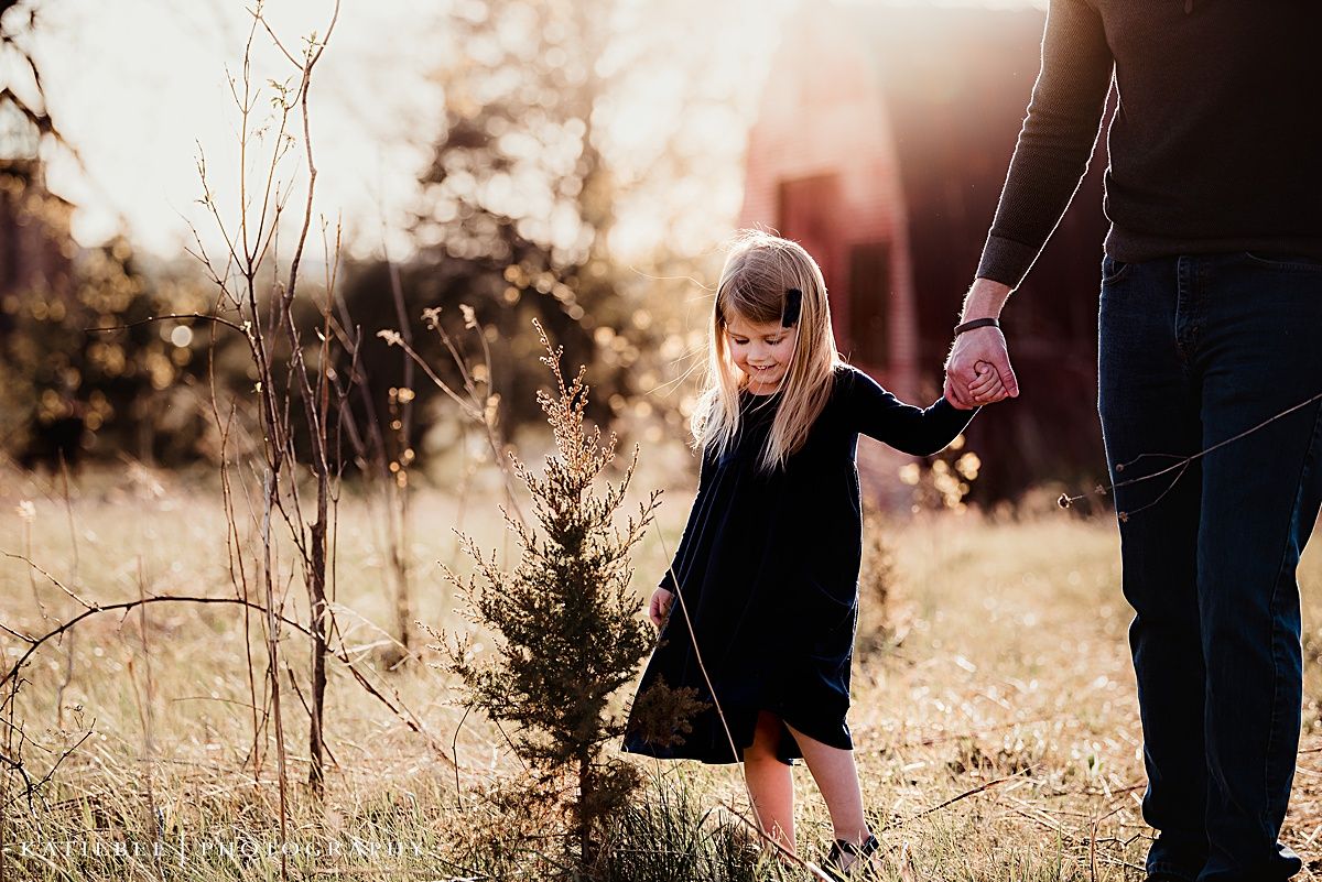 Child in black dress walking through sunlit field with adult.