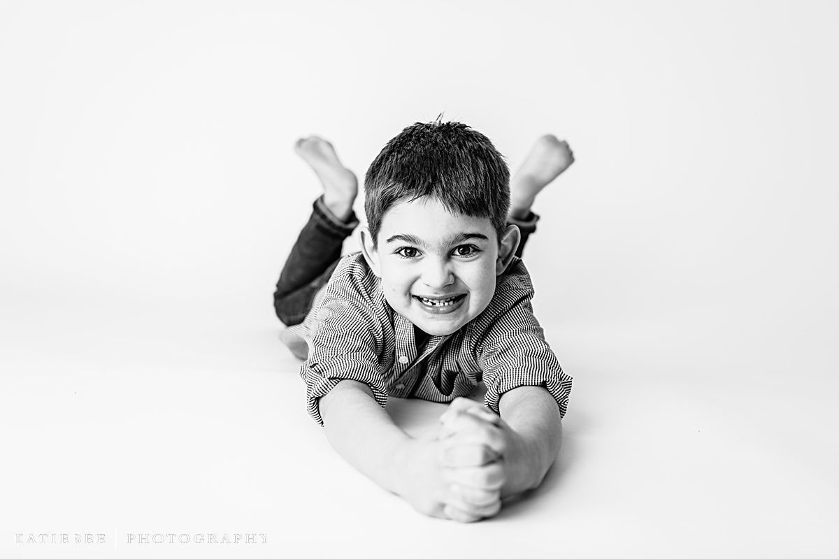 Child lying on stomach with raised feet in casual pose against white background.