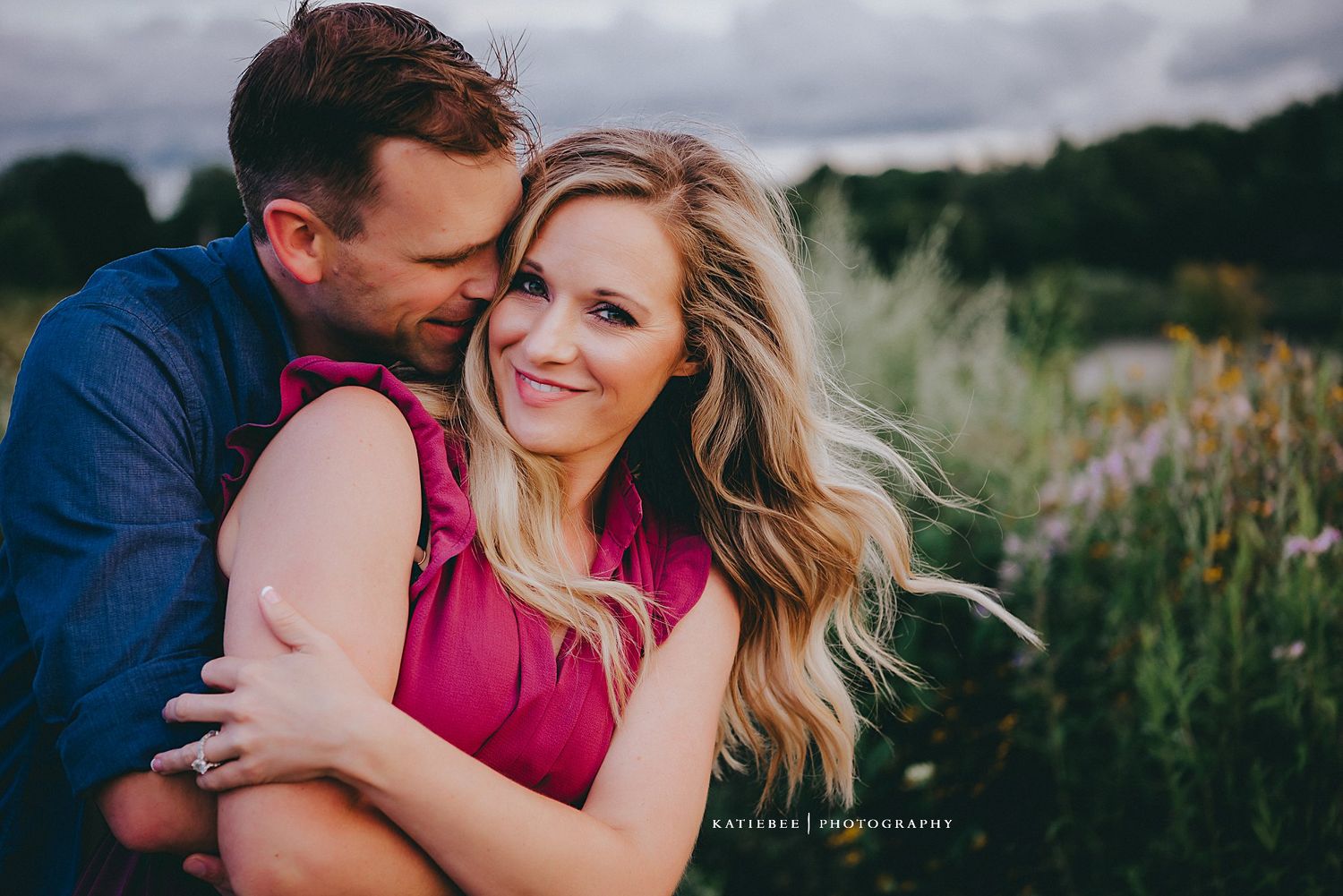 A joyful outdoor portrait of a couple embracing in casual attire against a natural landscape.