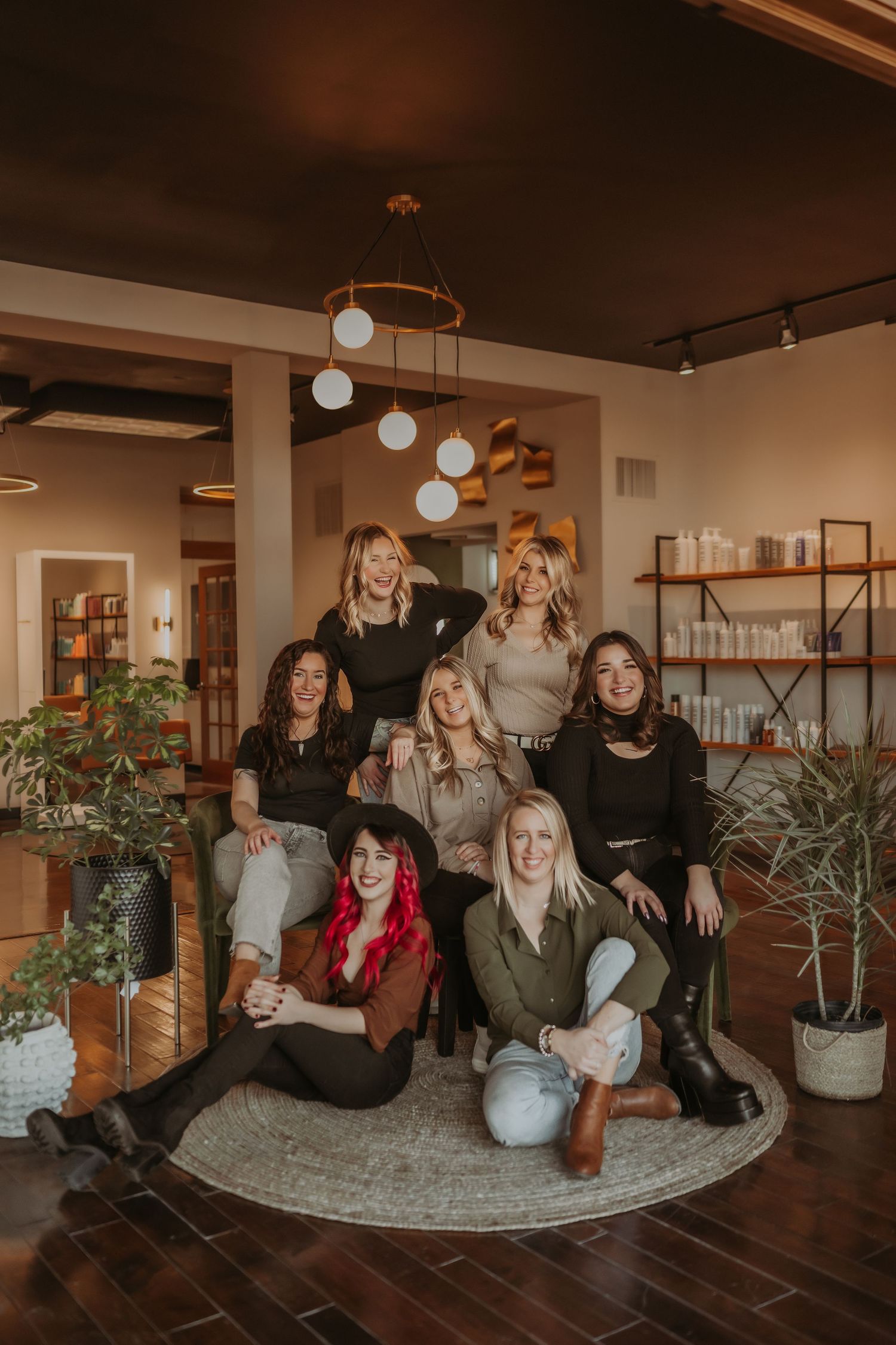 Group photo of friends sitting and standing in a modern salon interior with warm lighting and decorative globe pendant lamps.