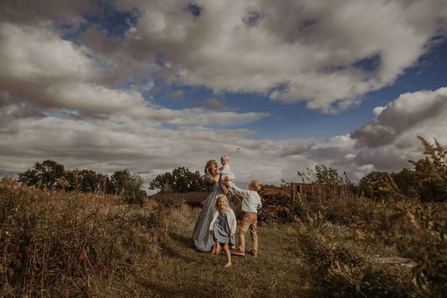 A candid family portrait on a hilltop with dramatic cloudy skies and wild grass in the background.
