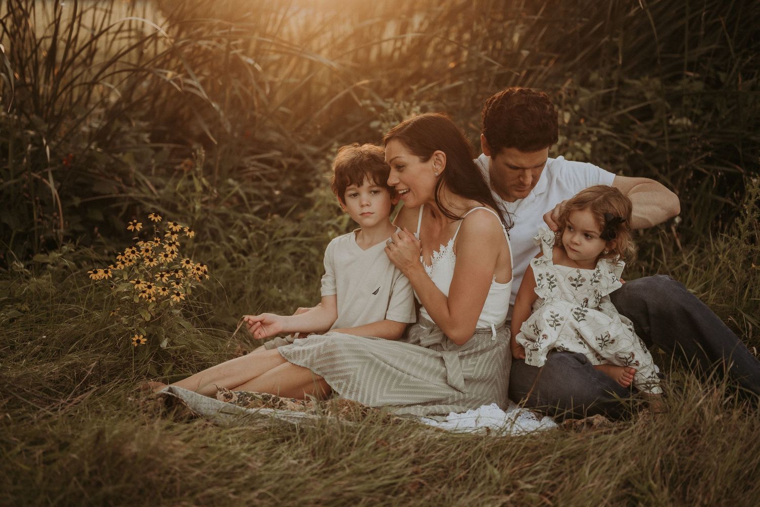 A family sits together on a blanket in a field during sunset.