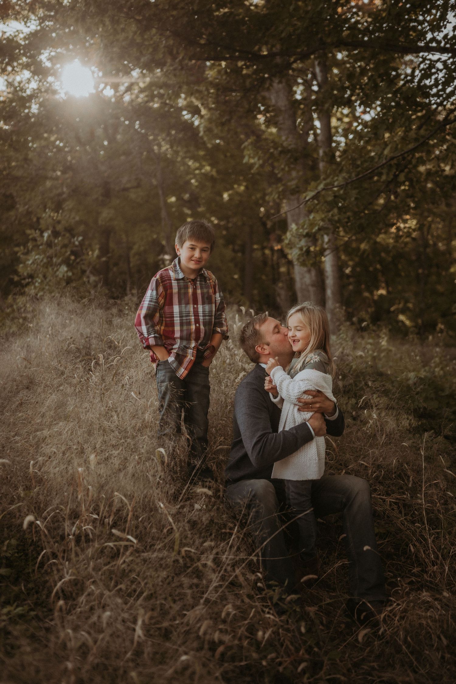 Playful family interaction photographed in rustic outdoor setting during golden hour.