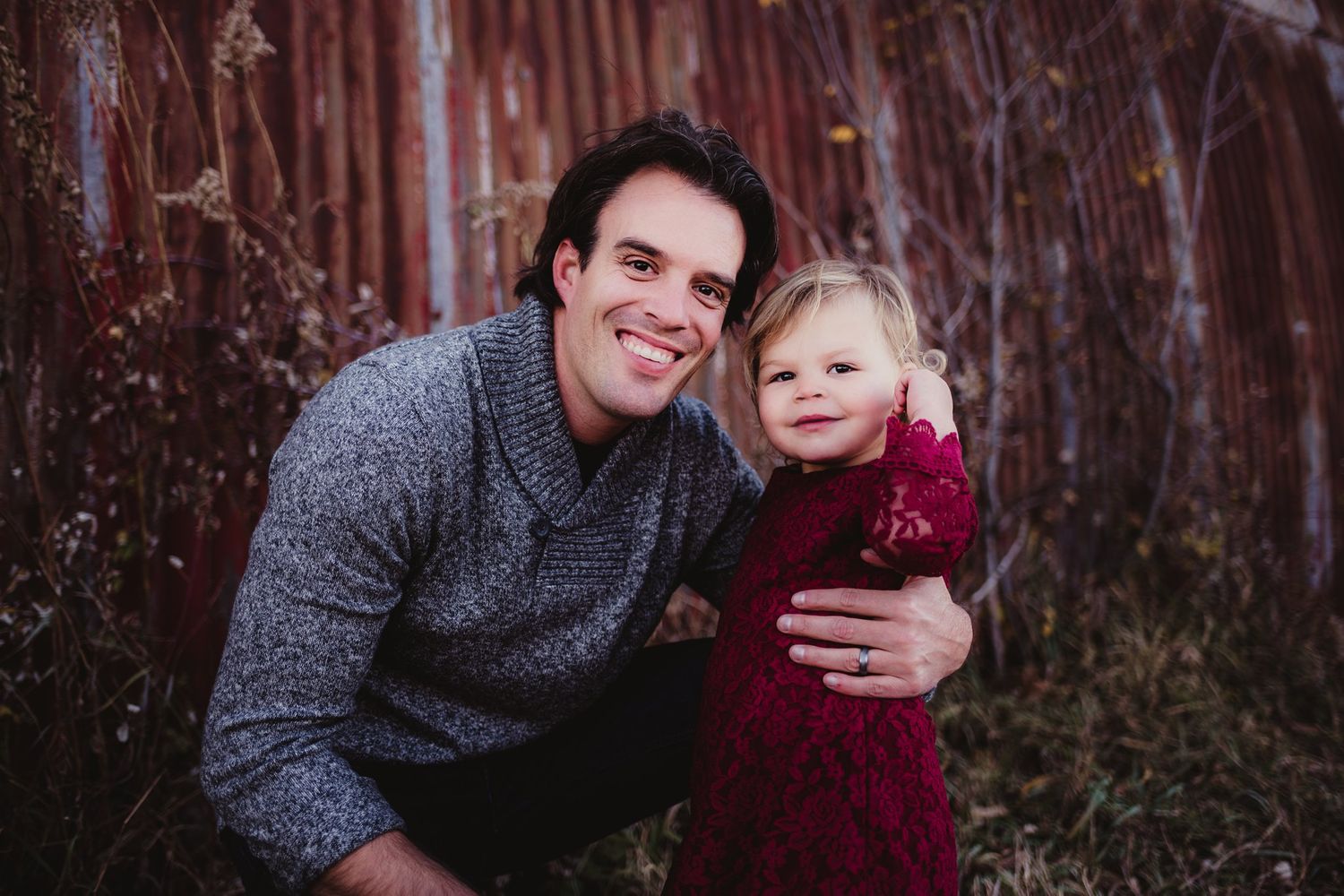 A heartwarming outdoor portrait against rustic red wall with burgundy and grey attire.