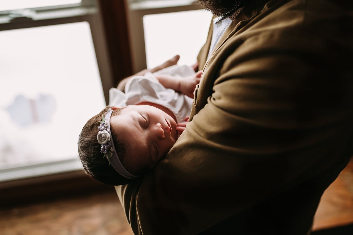Soft natural light illuminates a tender moment with a newborn wrapped in white.