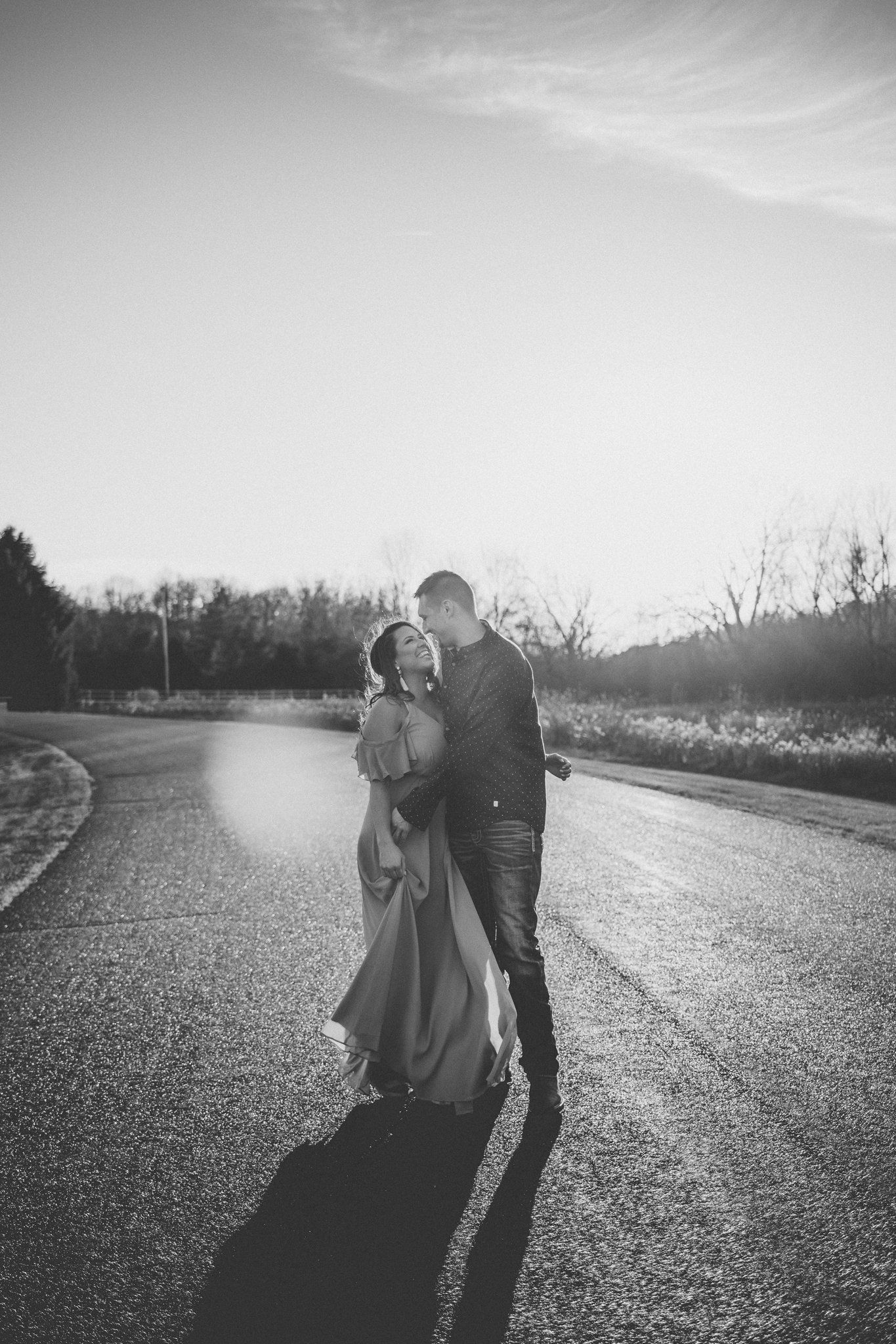 Black and white photo of couple embracing on wet road with dramatic lighting.