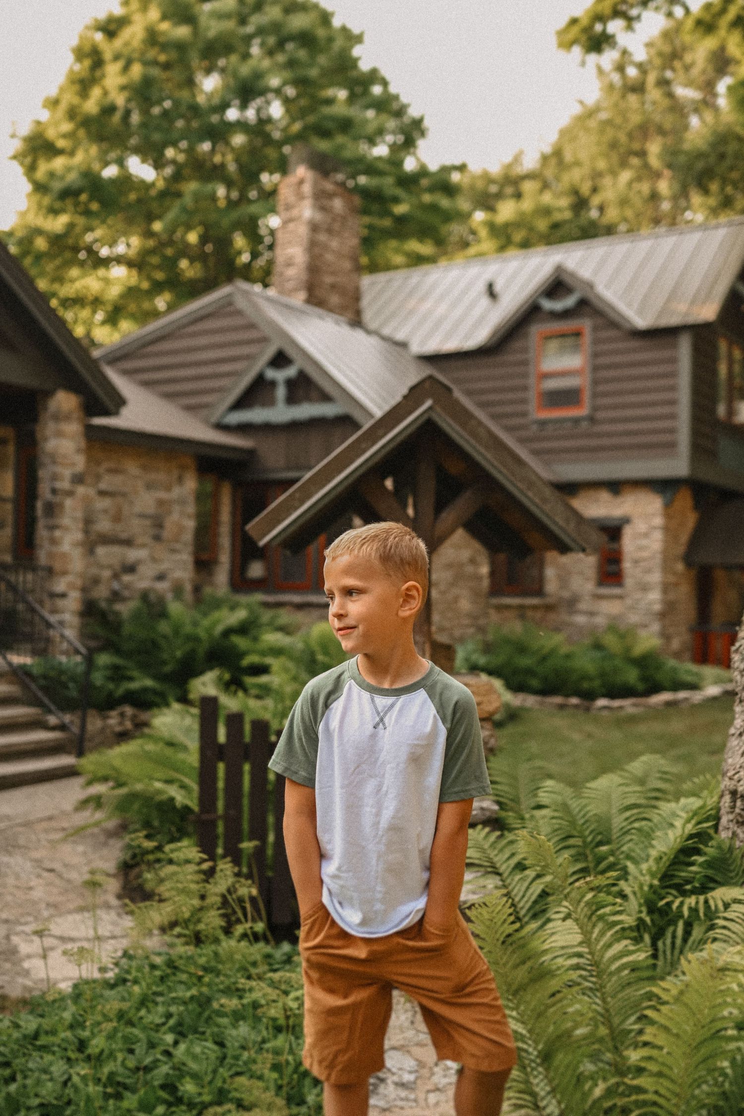 Casual outdoor portrait against rustic stone and wood cottage with ferns.