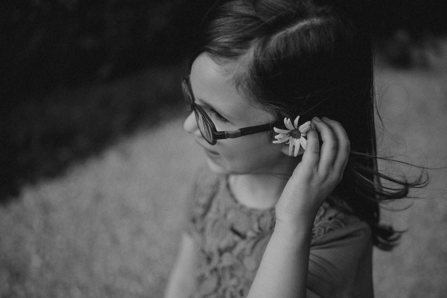 Black and white portrait showing someone adjusting glasses with a flower hair accessory.