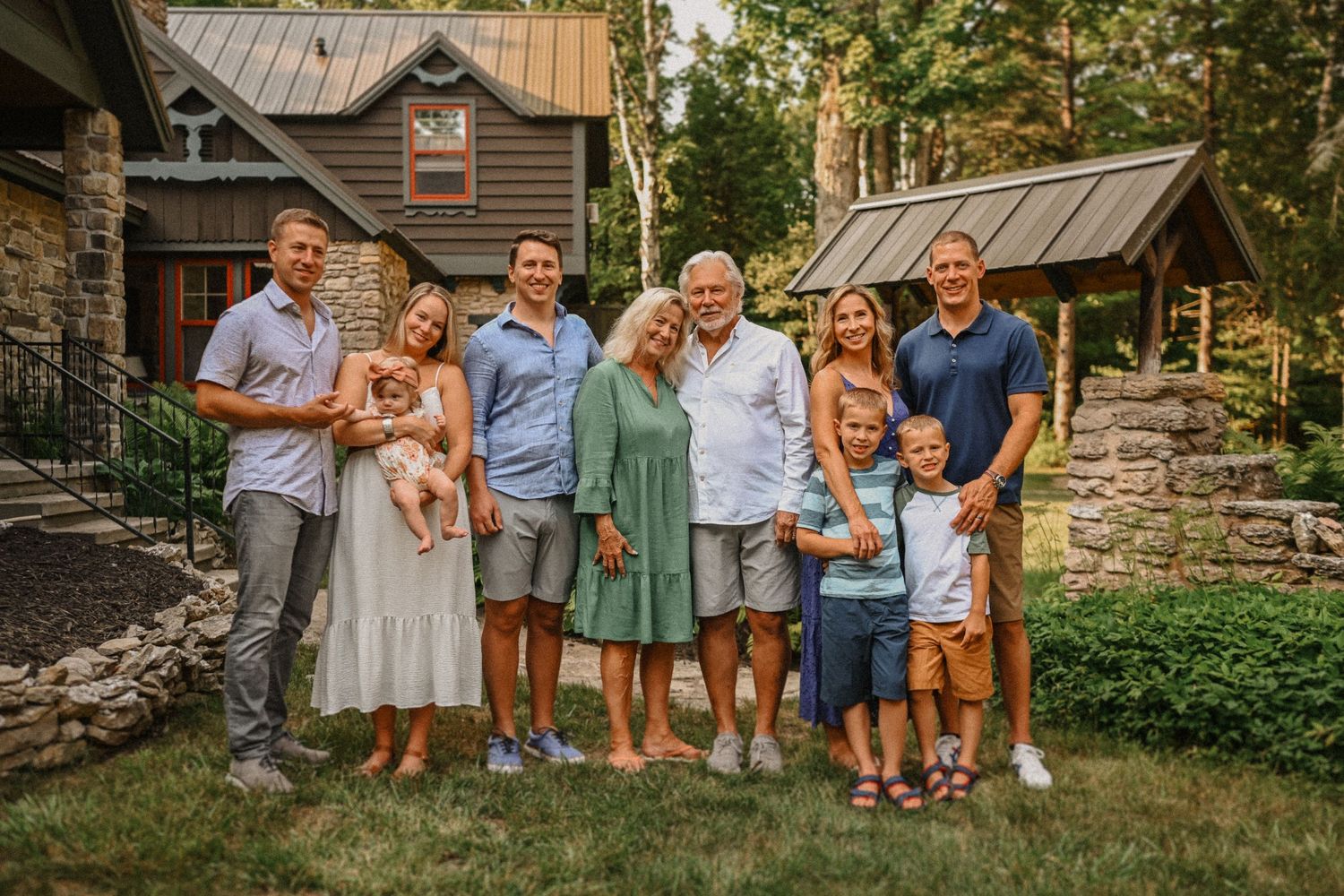 A multi-generational family portrait in front of a rustic stone house with wooden details.