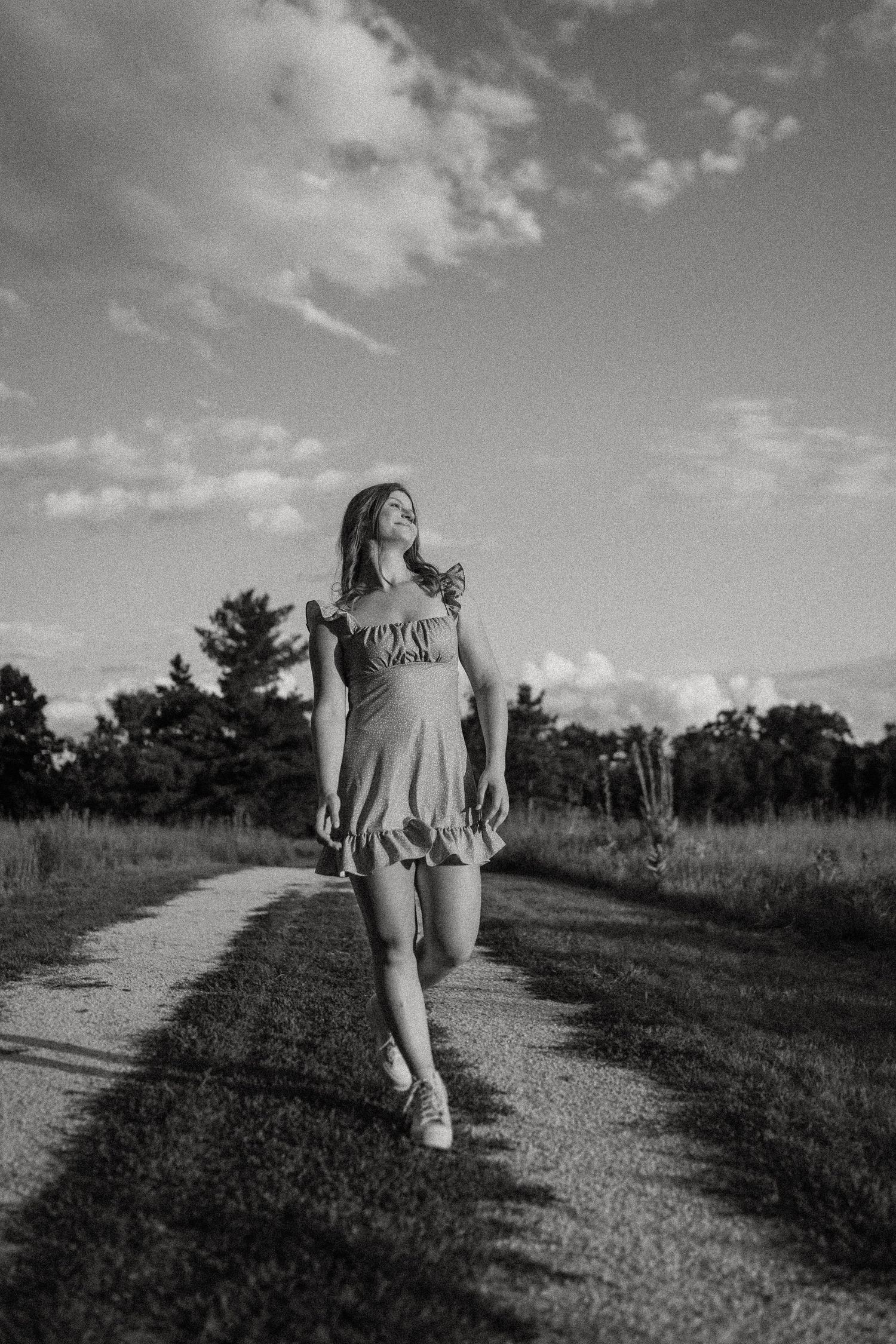 Black and white portrait along a peaceful country path under cloudy skies.