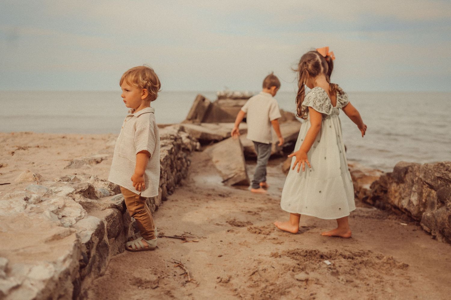 Children explore rocky formations along a scenic beach during golden hour.