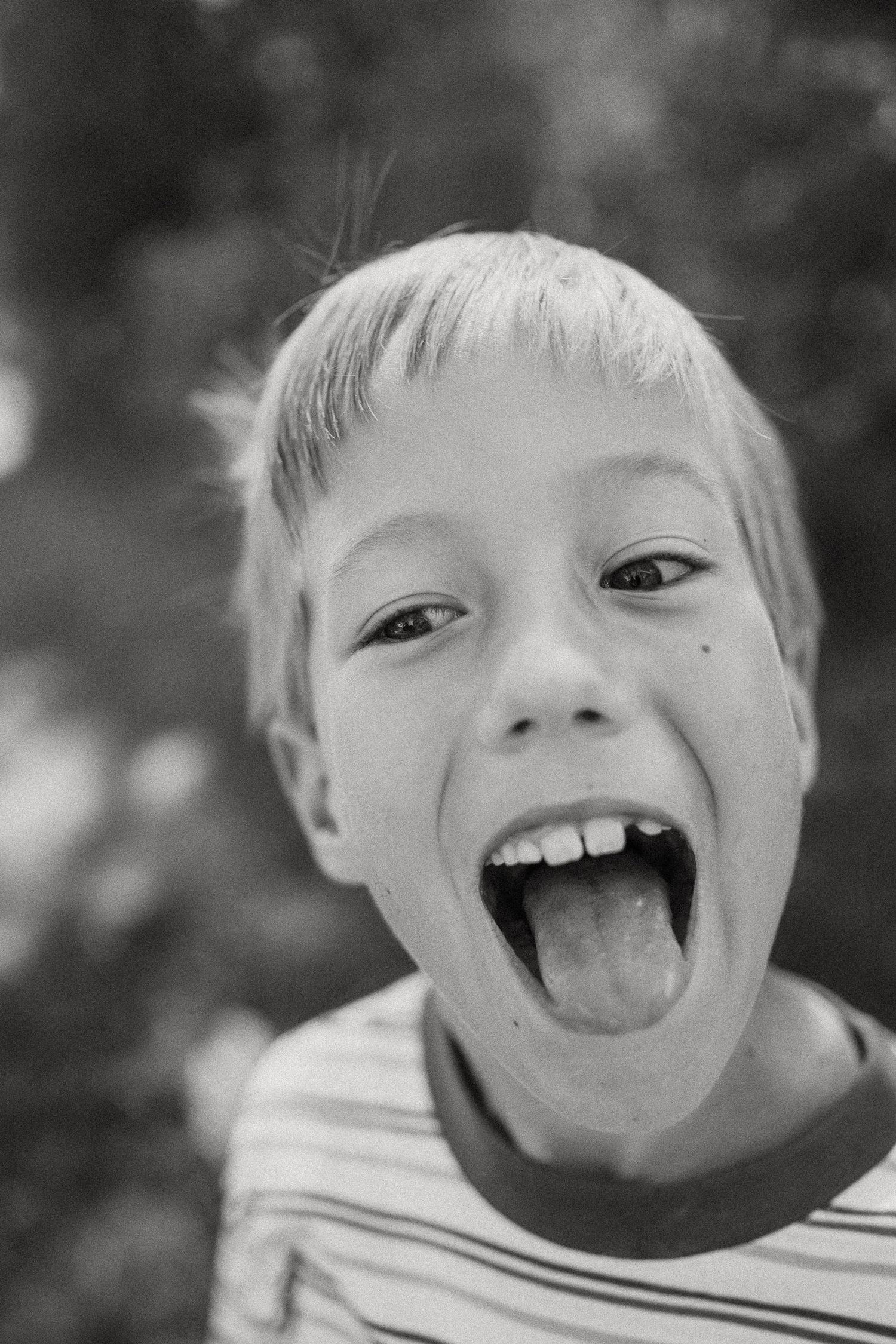 Black and white close-up of a playful young boy sticking his tongue out at the camera.