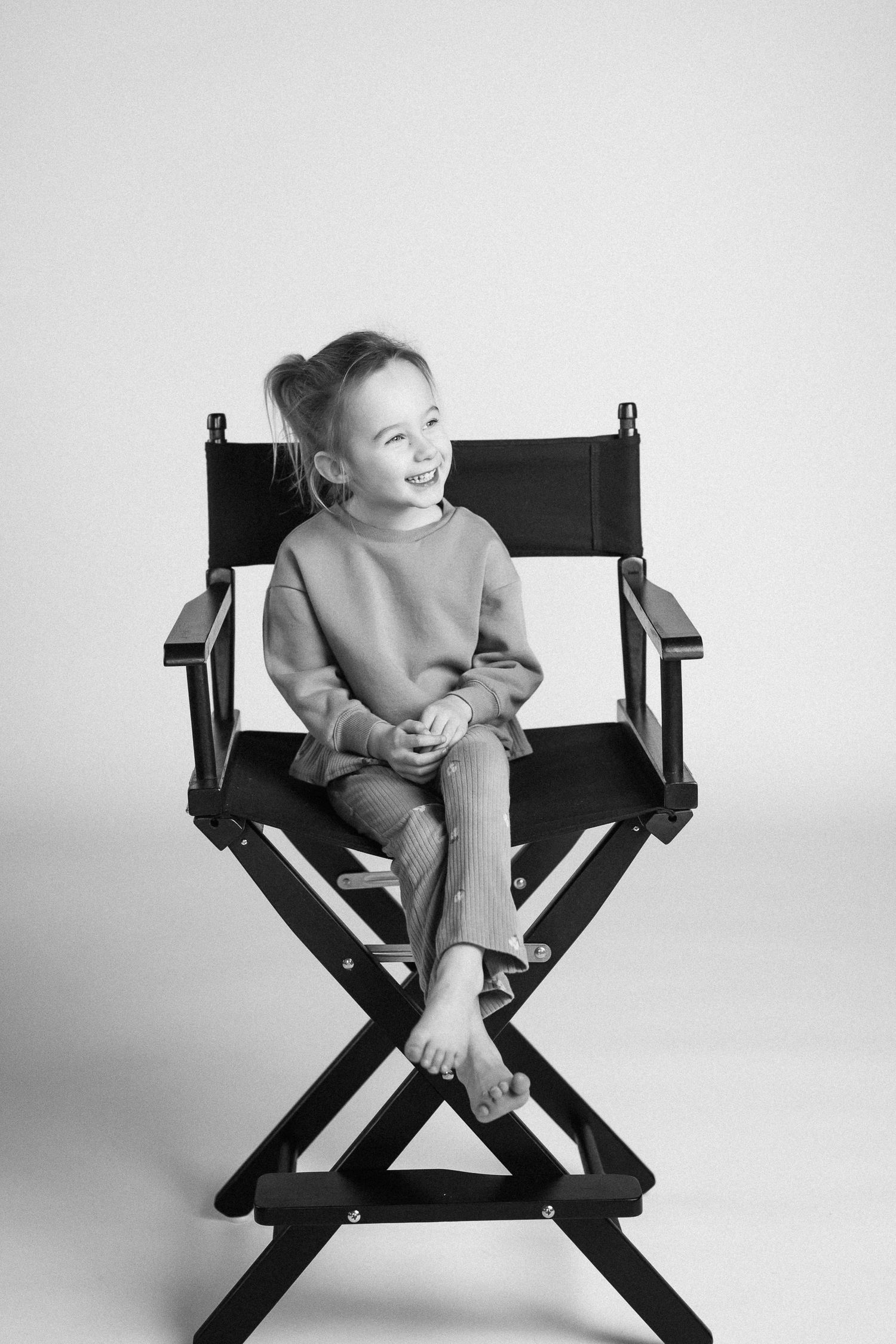 Series of black and white photos showing a child sitting and playing in a director's chair.