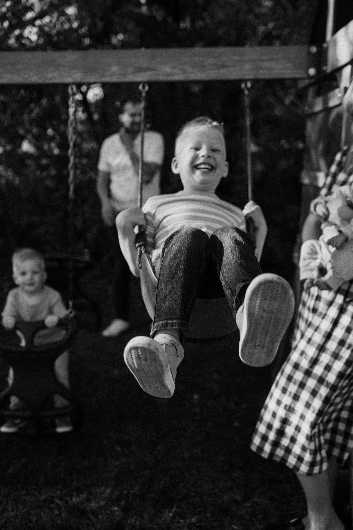 Laughing boy swinging joyfully outdoors in black and white family photo.