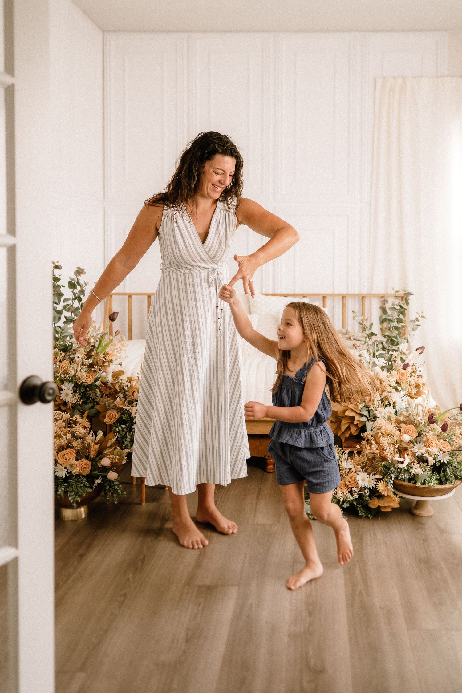 A parent and child dancing together in a bright room decorated with floral arrangements and autumn colors.