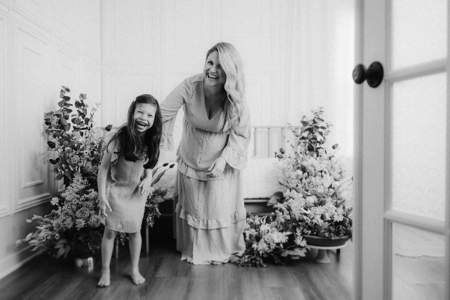 A mother and young child share a joyful moment dancing together in a bright room decorated with holiday greenery.