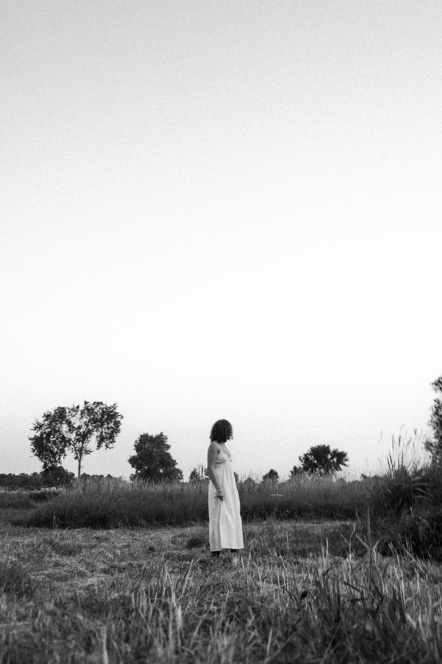 A silhouetted figure stands alone in a misty field during twilight, captured in black and white.