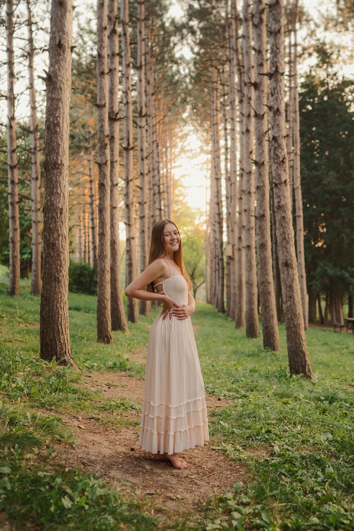 A dreamy series of photos in a pine forest features a flowing white dress against tall trunks at golden hour.