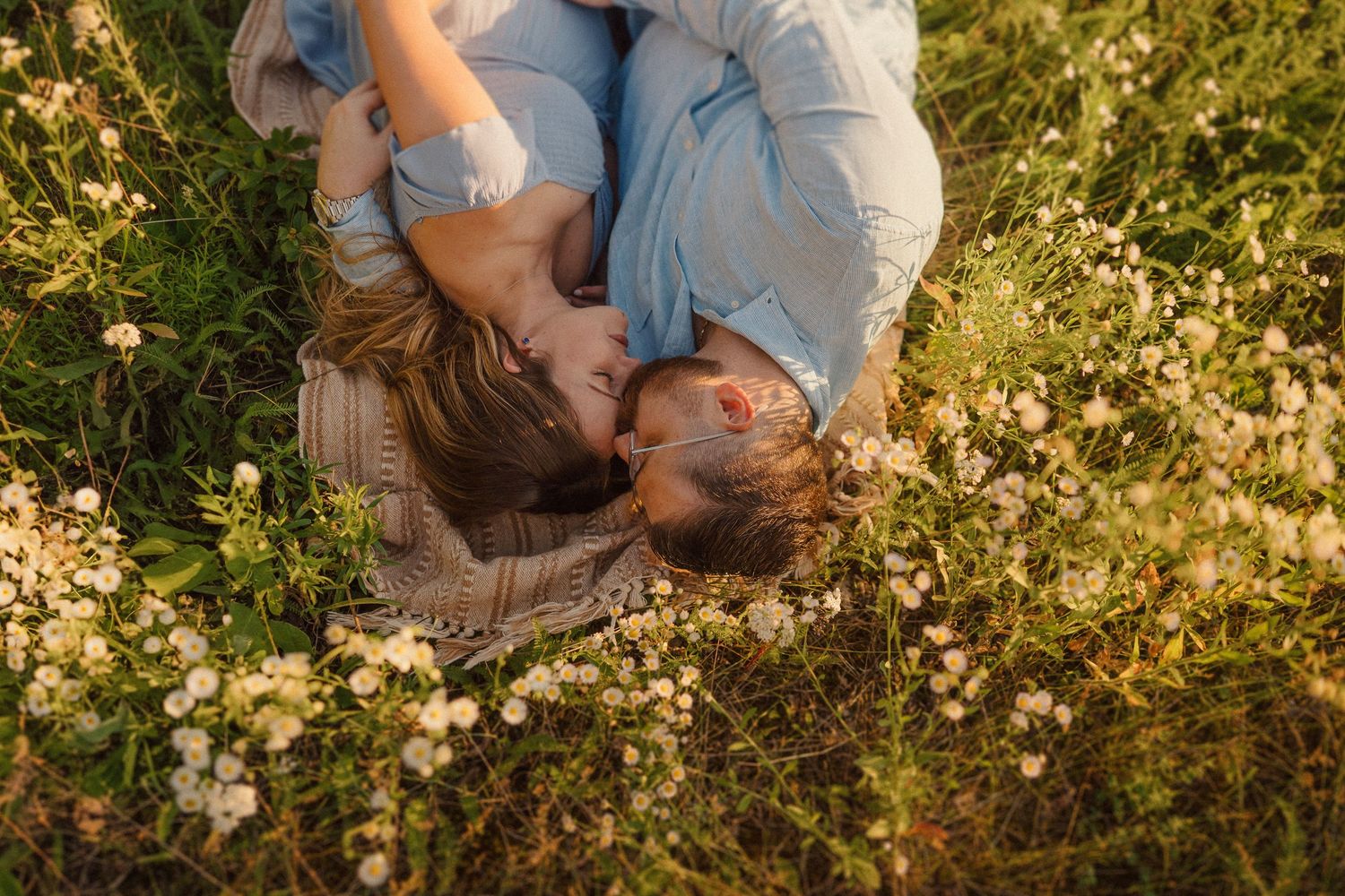 Golden sunlight illuminates an intimate couple's portrait session among blooming wildflowers in a field.