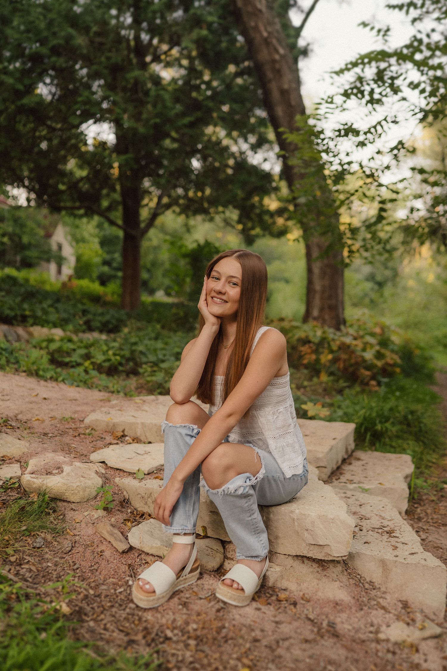 Someone sits casually on stone steps surrounded by lush greenery in a natural outdoor setting.