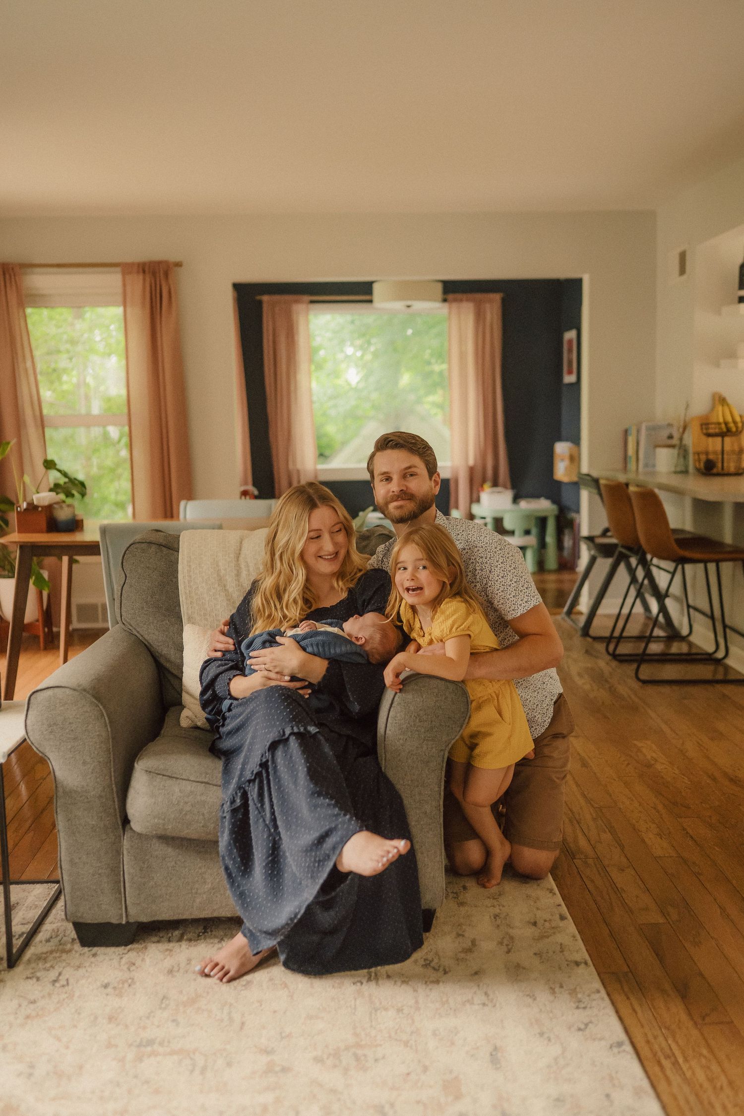 A warm family photo capturing an intimate moment together on their living room couch with hardwood floors.