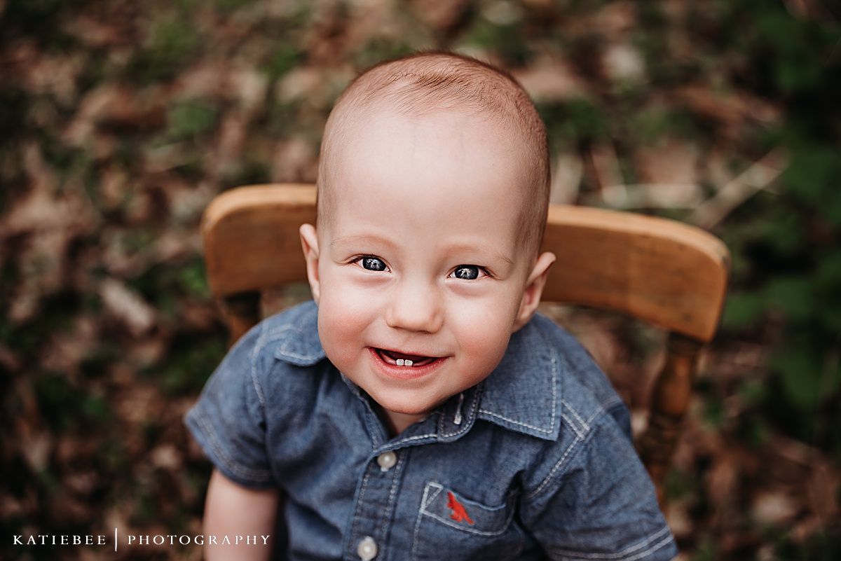 Close up portrait of happy baby in denim shirt sitting in wooden chair.