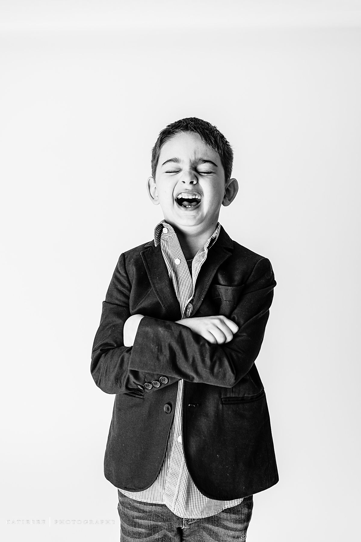 Monochrome portrait of laughing child in dark blazer with crossed arms.