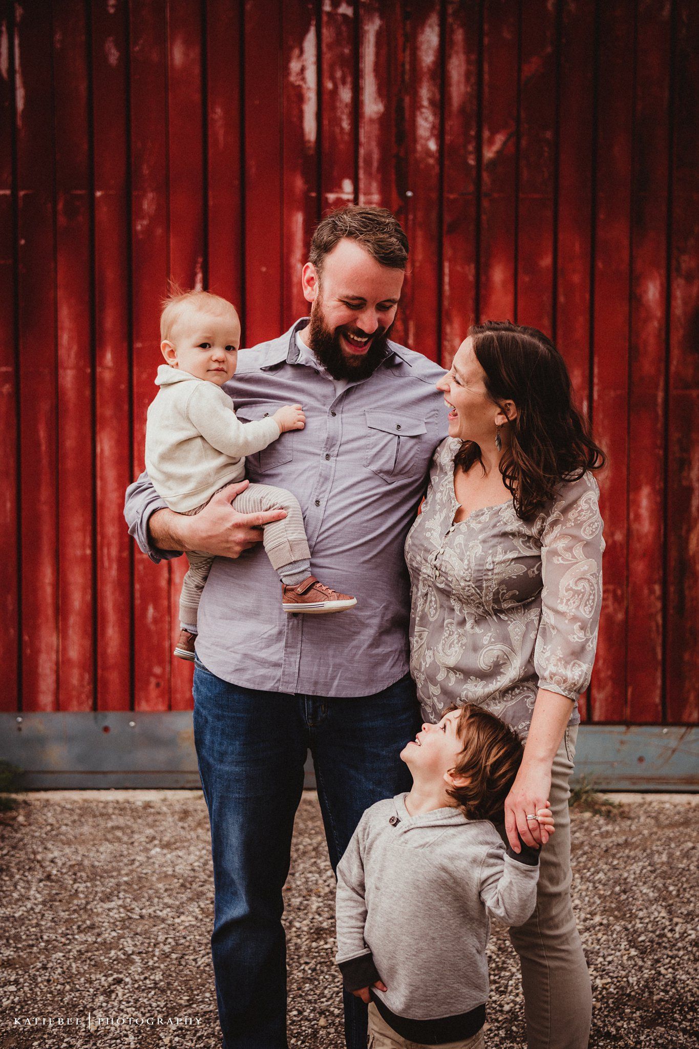 Family poses together against rustic red barn wall during photo session.
