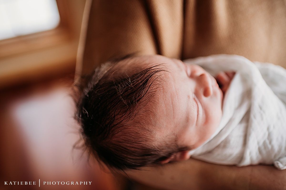 Close up of a sleeping newborn baby wrapped in white blanket.