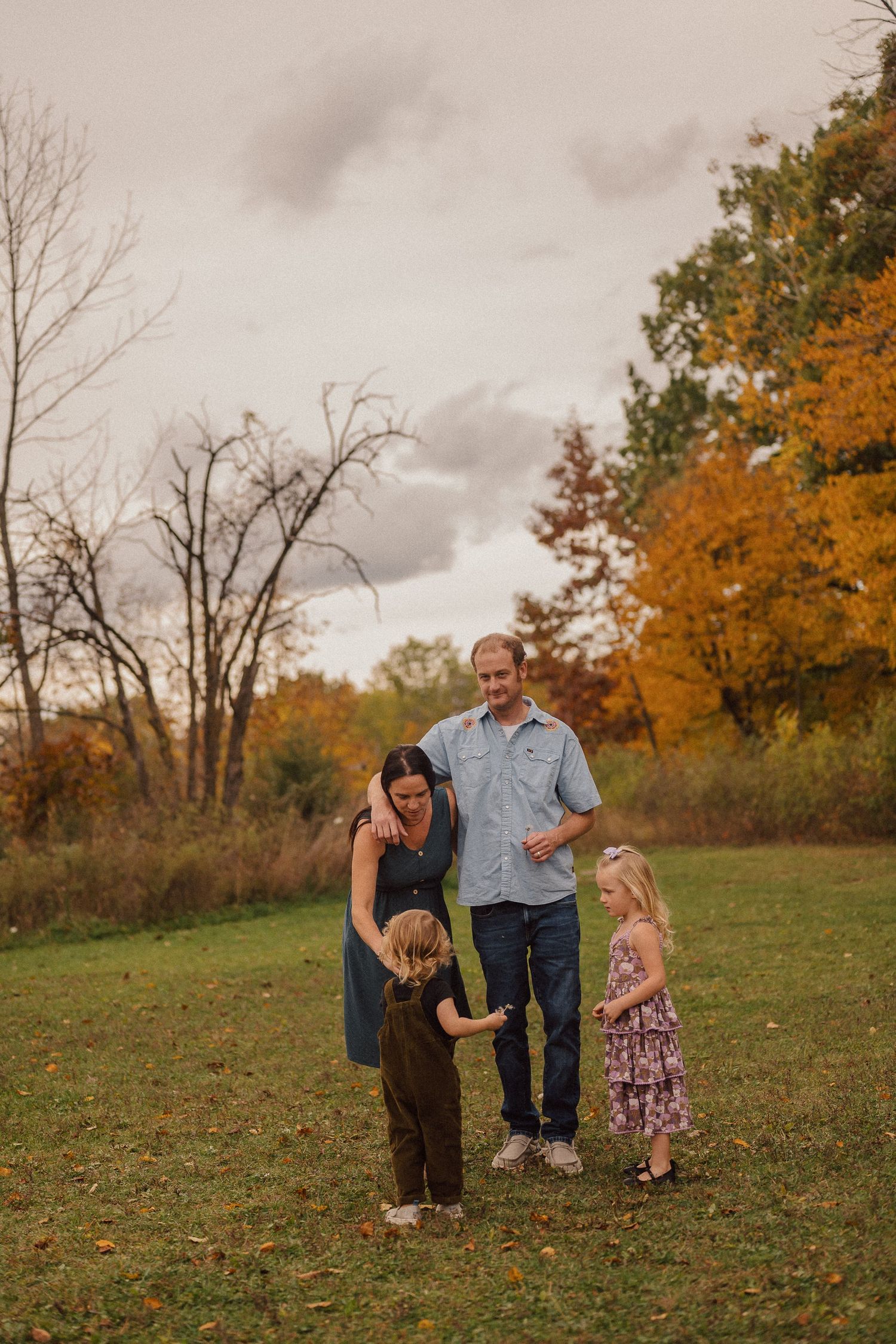 A family enjoying a fall day together on a grassy hillside with autumn trees in the background.
