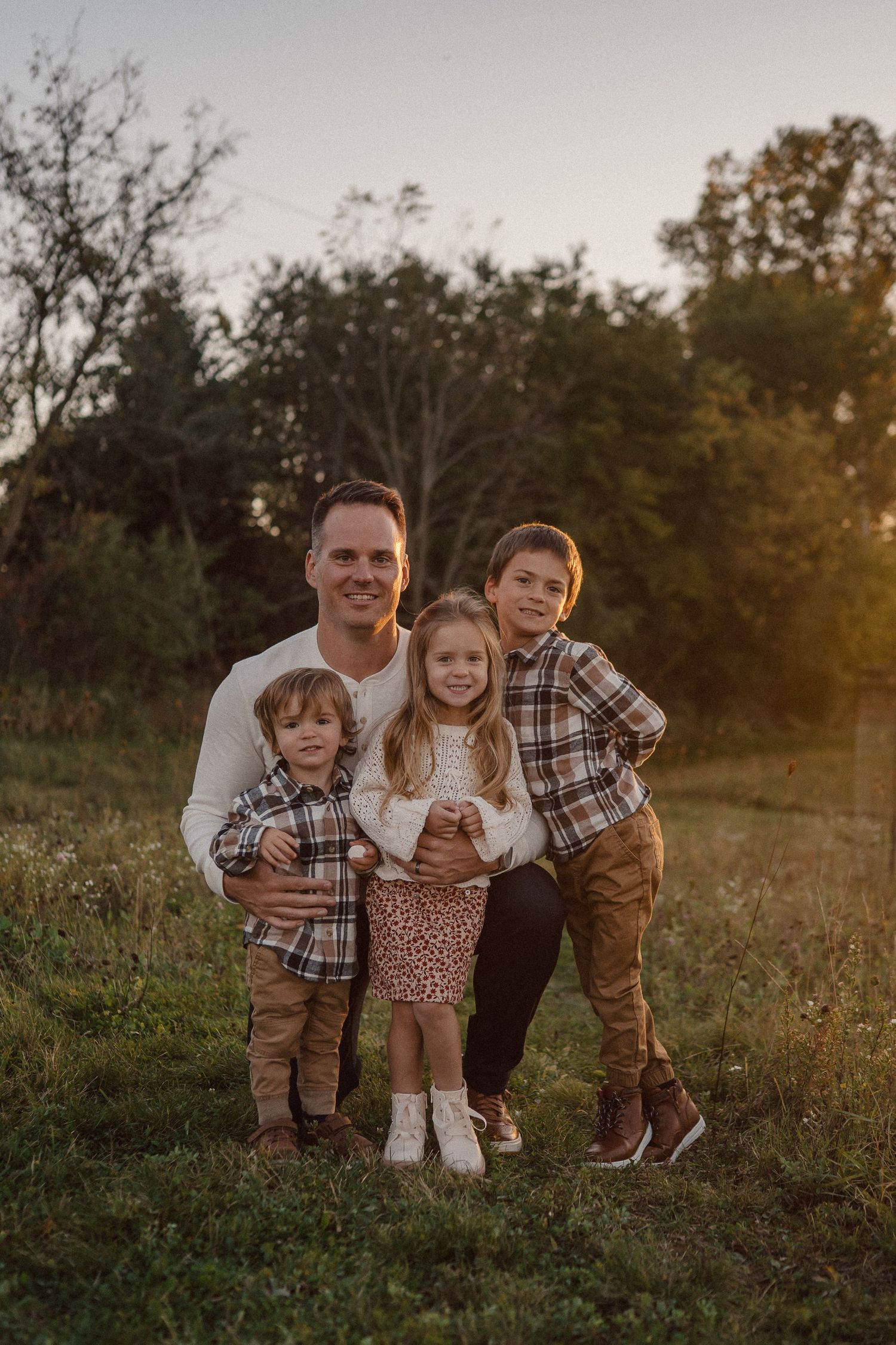 A family group poses together in a natural field setting during sunset.