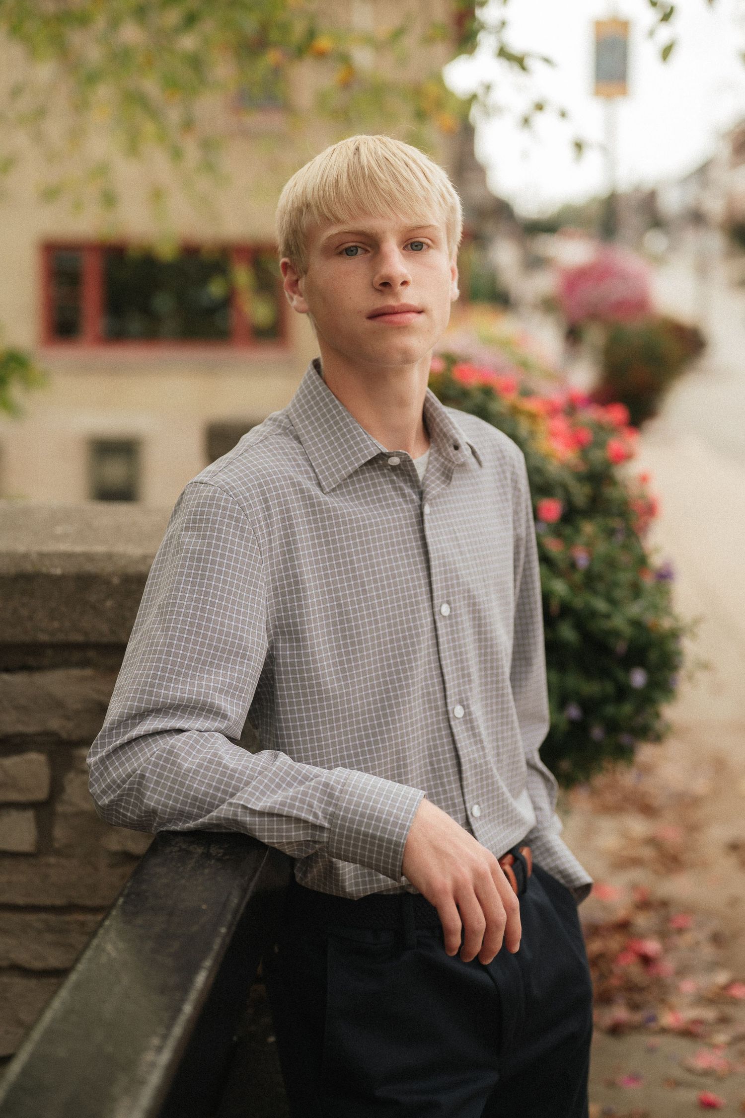 Person in checkered shirt poses against stone wall with blooming red flowers and autumn leaves.