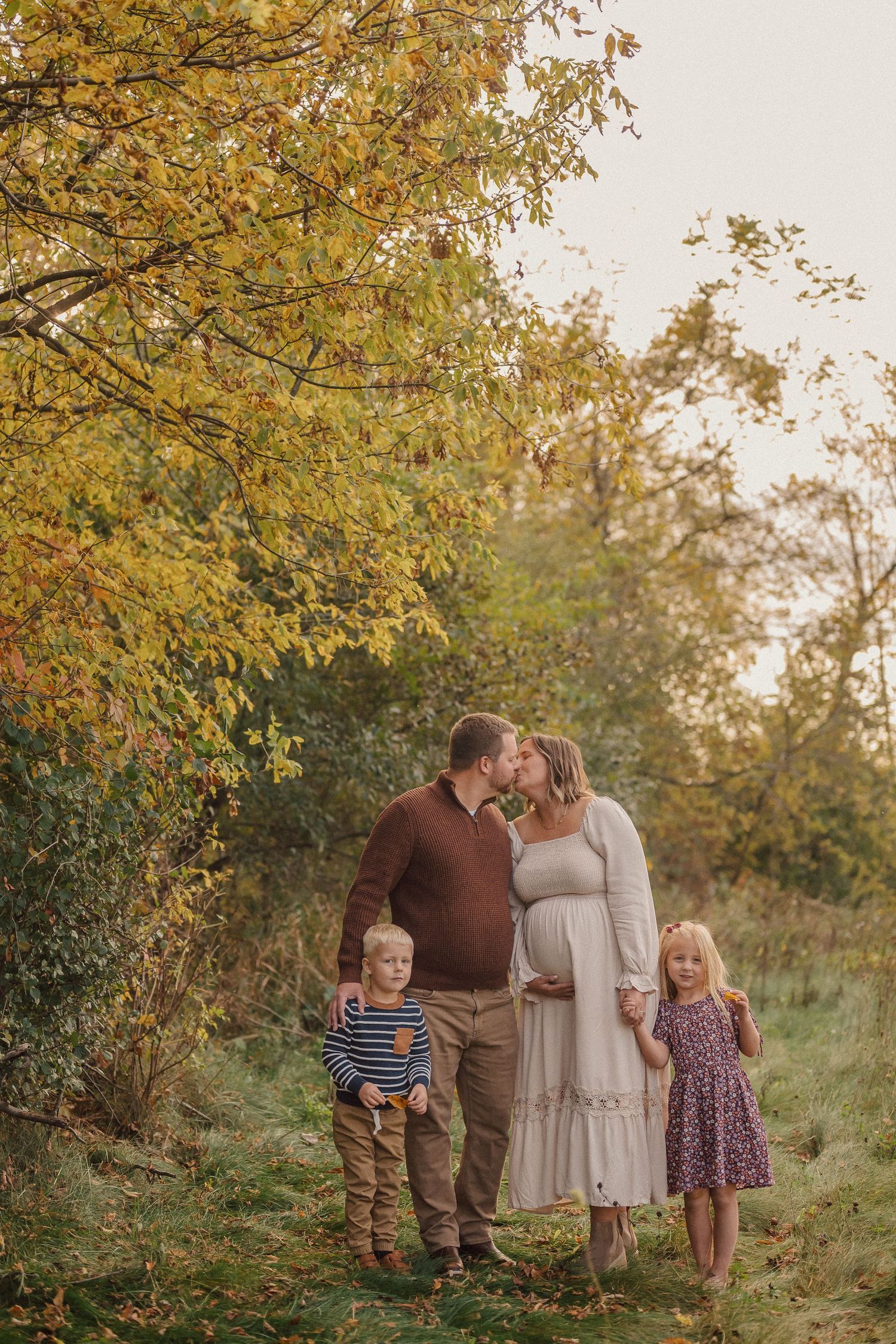 Family enjoying a tender moment together in an autumn field with golden leaves overhead at sunset.