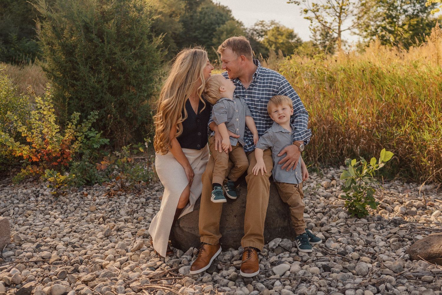 A family sits together on rocky terrain during sunset while sharing an intimate moment outdoors.
