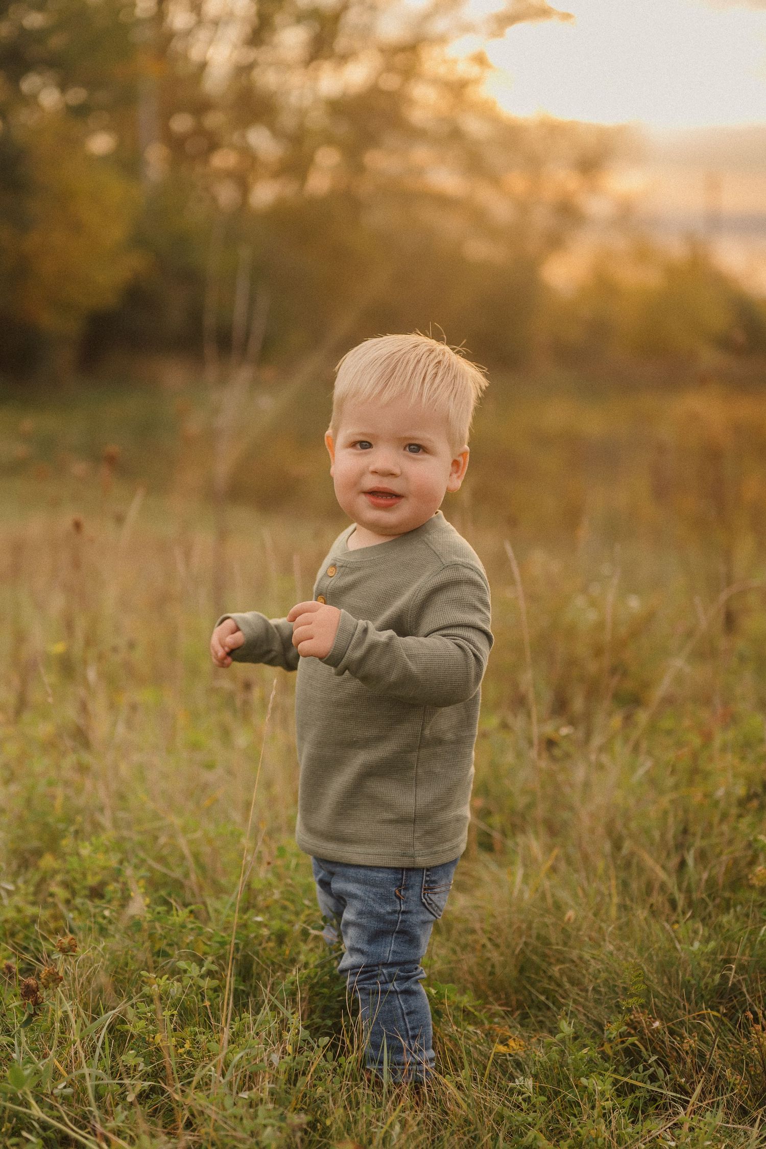 Small child exploring a golden autumn field at sunset wearing a gray sweater and jeans.
