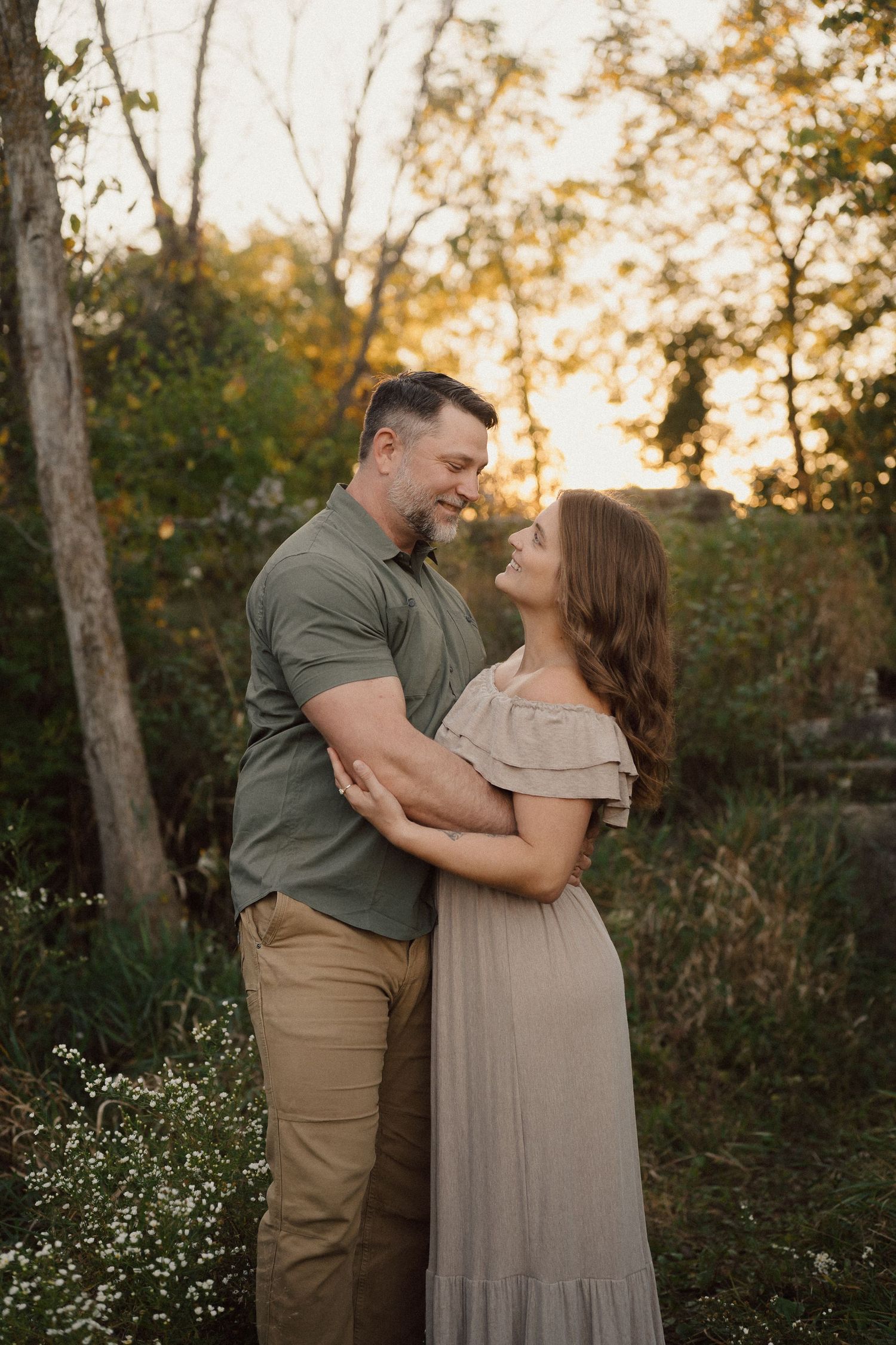 A romantic couple shares tender moments in a wooded area during golden hour sunset.