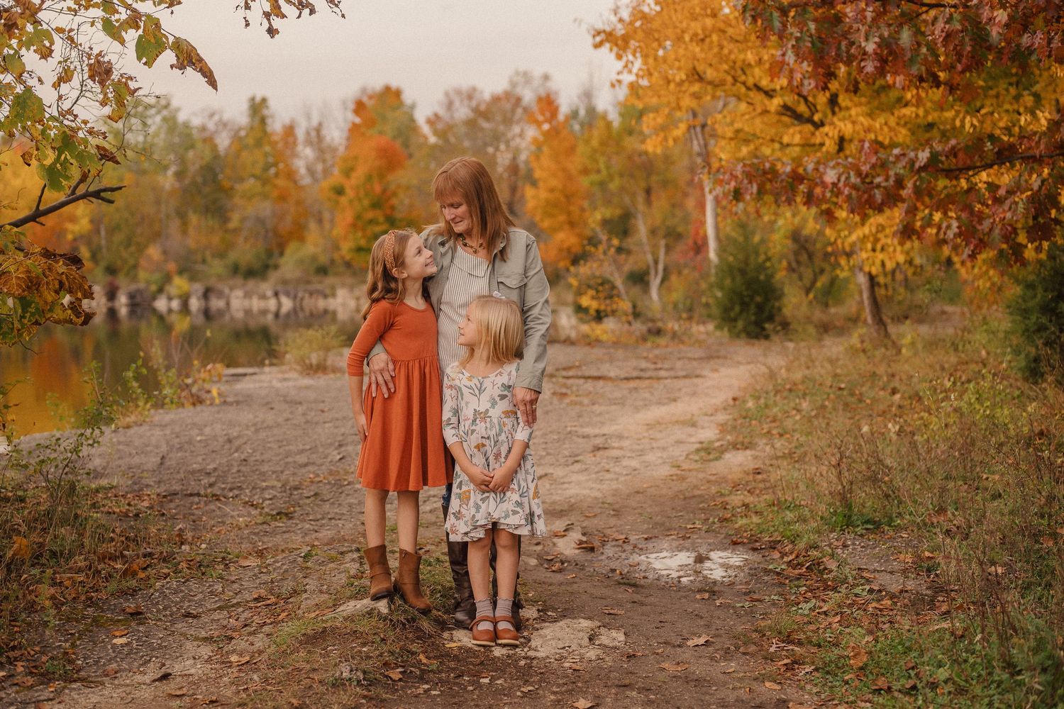 Two people walk together on a dirt path surrounded by vibrant autumn foliage and golden afternoon light.