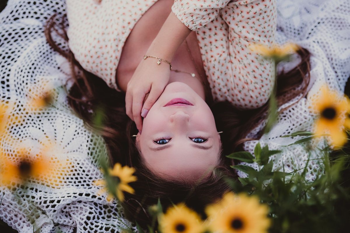 Artistic overhead shot lying on lace blanket surrounded by yellow sunflowers in garden.