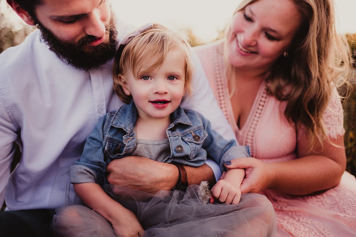 Close-up family portrait with white shirt and pink dress against natural background.