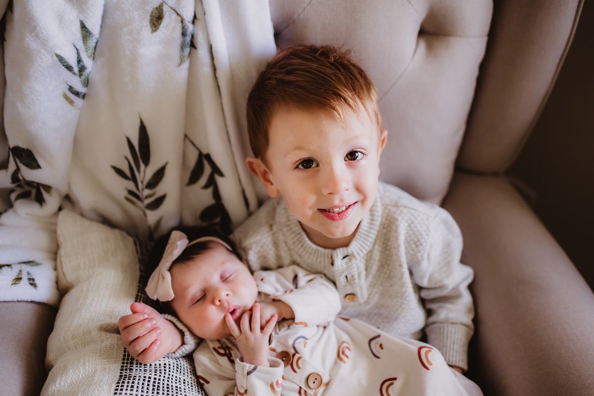 Siblings sharing a tender moment on tufted chair with floral pattern cushions.