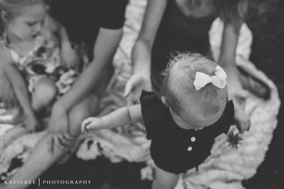 Family shares laughter and embraces while sitting together on a blanket in evening sunlight.