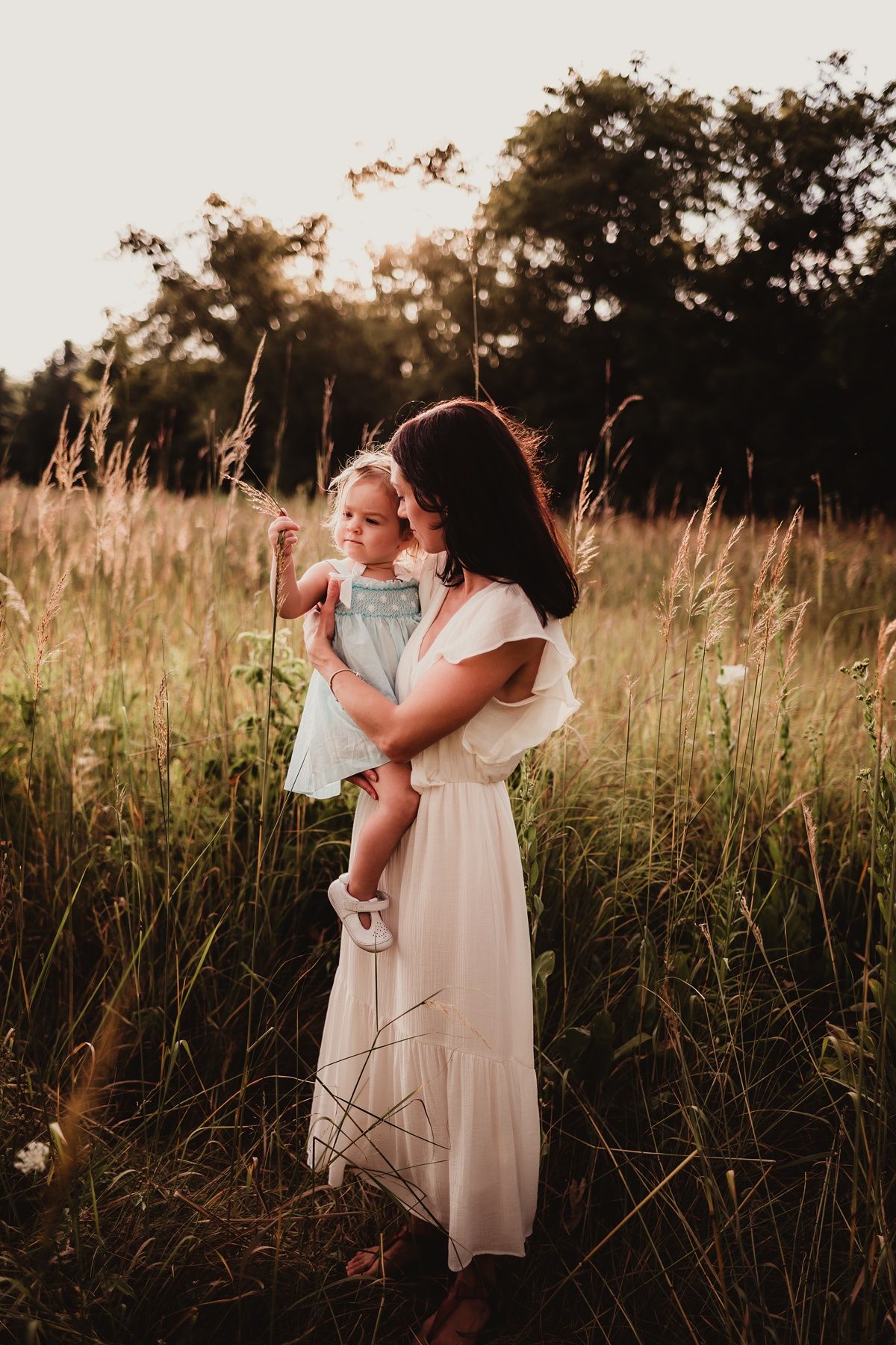 Mother and child share tender moment in sunlit meadow at dusk.