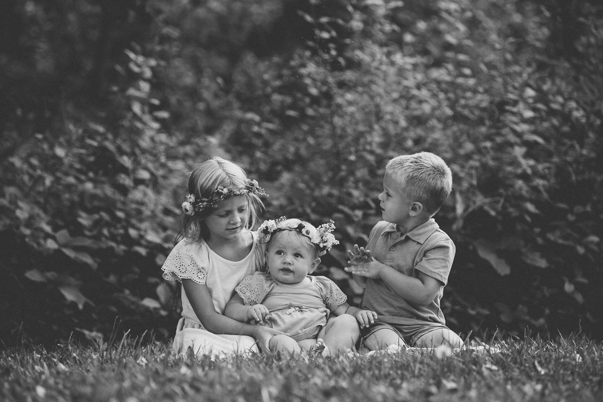 Black and white portrait of three children sitting together on grass outdoors.