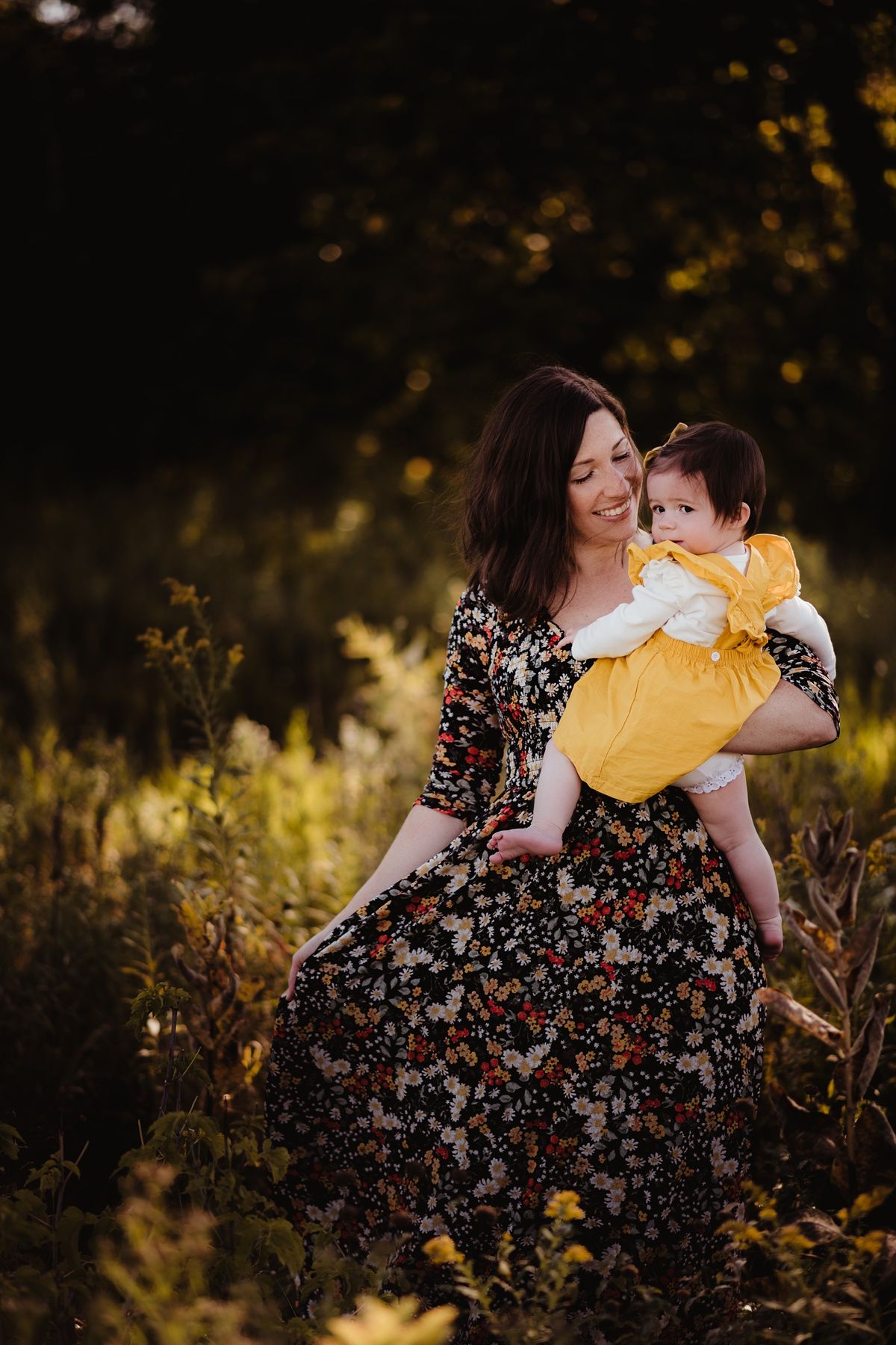 Outdoor portrait in golden light with adult in floral dress holding baby in yellow outfit.
