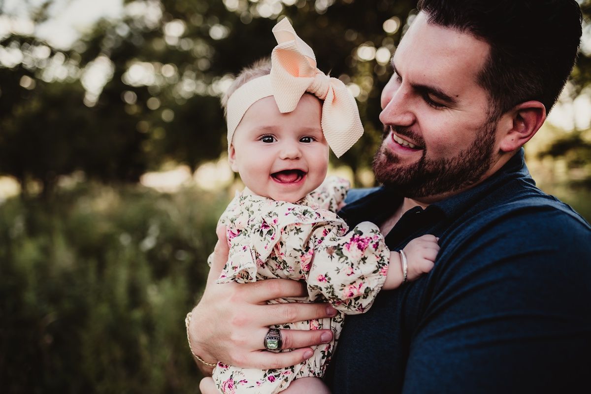 Happy moment captured between parent and baby with bow in wildflower field.