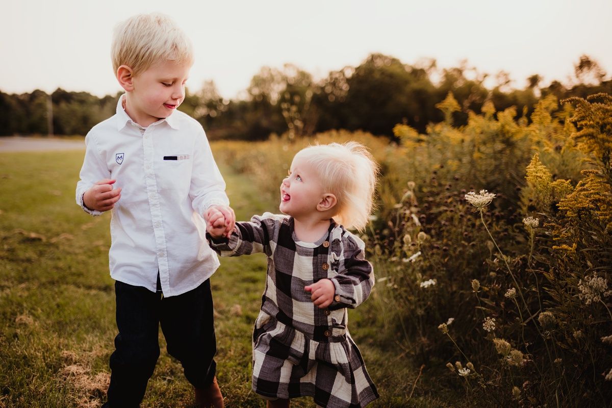 Children explore wildflowers together in a field during sunset.
