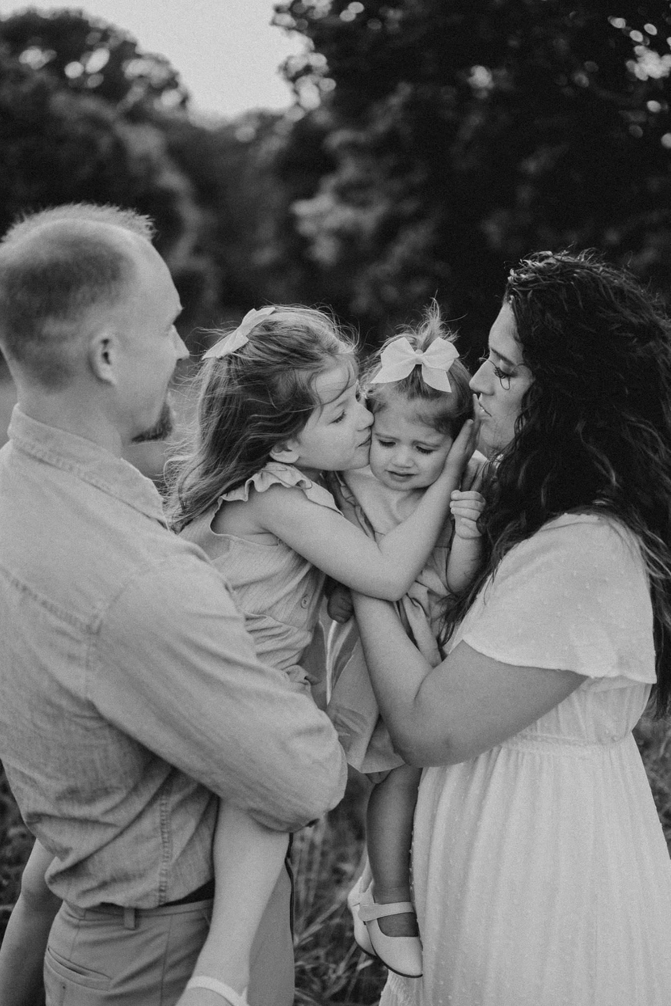 A tender family moment captured in black and white as parents hold and embrace their young children outdoors.