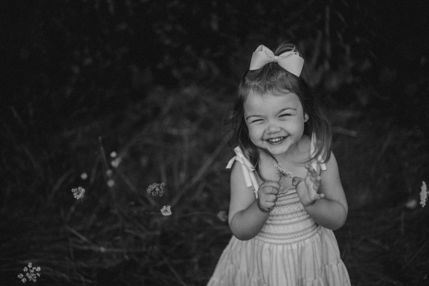A black and white portrait captures a joyful moment of a child in a dress outdoors.